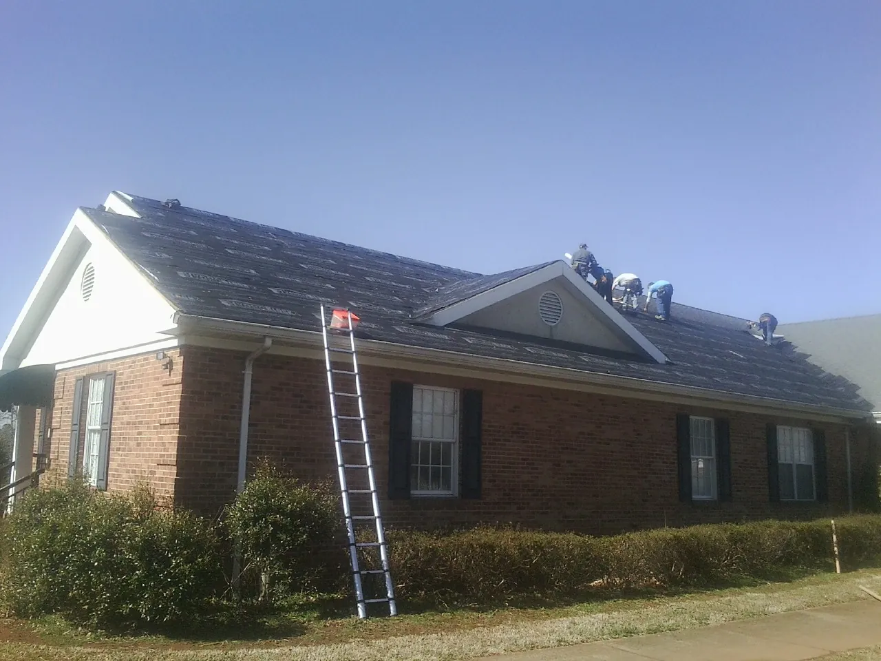 Crew tearing shingles off a brick ranch roof with a ladder set — Metal Roof Repair work by our crew in Afton