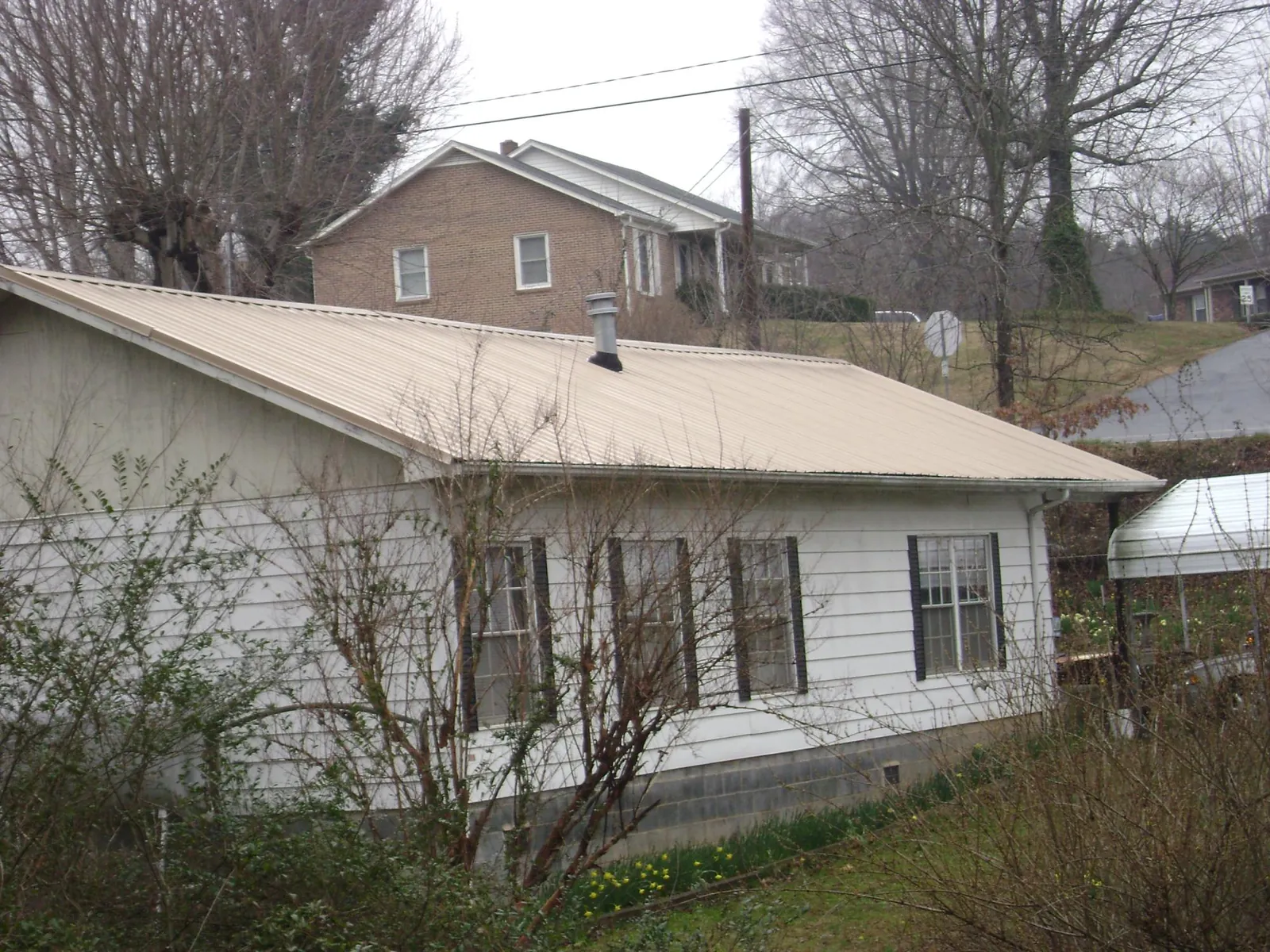 Tan metal roof on a white sided house set into a hillside — Commercial Roofing by Roofing Brothers in Afton